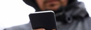 Kapüşonlu adam akıllı telefonlara bakıyor.