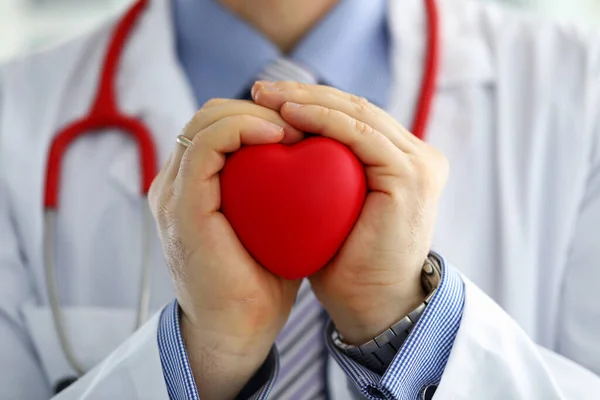 Médico masculino manos sosteniendo y cubriendo corazón de juguete rojo — Foto de Stock