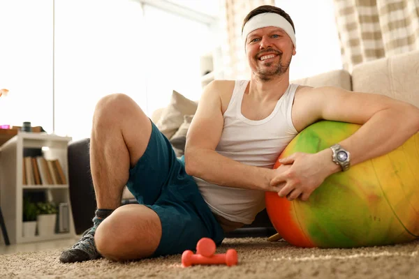 Man sitting at home carpet near ball and dumbbells — Stock Photo, Image