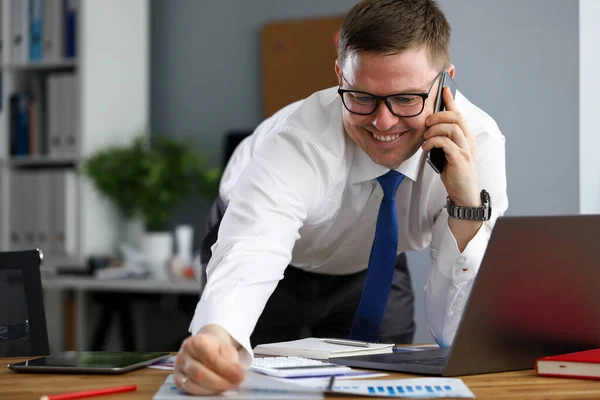 Radostný muž v kanceláři mluví po telefonu poblíž notebooku — Stock fotografie