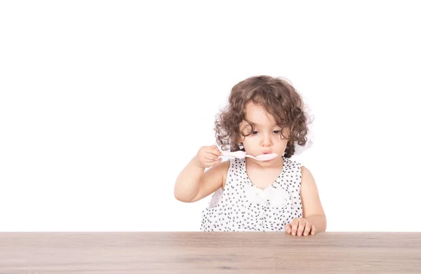 Kız boş masada oturan bir kaşıkla yemek — Stok fotoğraf