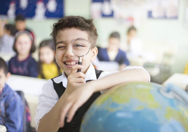 Leuke jongen student op zoek globe met Vergrootglas — Stockfoto