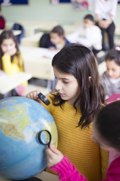 Девушка студентка смотрит на карту мира с увеличителем в классе — стоковое фото
