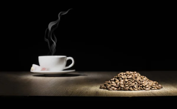 Taza de café al vapor en la mesa de madera con la pila de granos de café — Foto de Stock