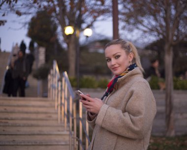 Genç kız elinde telefonla dışarıda poz veriyor.