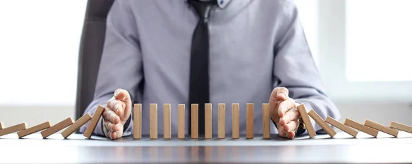 İşadamı domino etkisini önlemek için blokların düşmesini engelliyor.