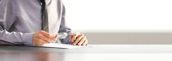 Kravatlı bir işadamı, büyüteçle bir belgeyi inceliyor. Kontrat imzalama kavramı