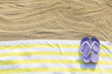 Sarı havluda mor terlikler. Kumsalda güneşlenme konsepti
