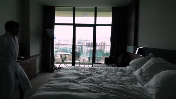 Lycklig ung Man hoppar på sängen på hotellet i badrock — Stockvideo