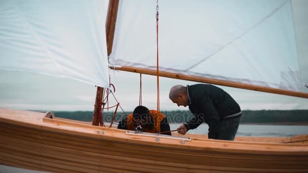 Wood sailboat with two men working with sail. — Stock Video