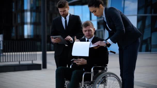 Un homme d'affaires en fauteuil roulant avec des collègues à l'extérieur d'un immeuble de bureaux discute d'affaires et d'affaires . — Video