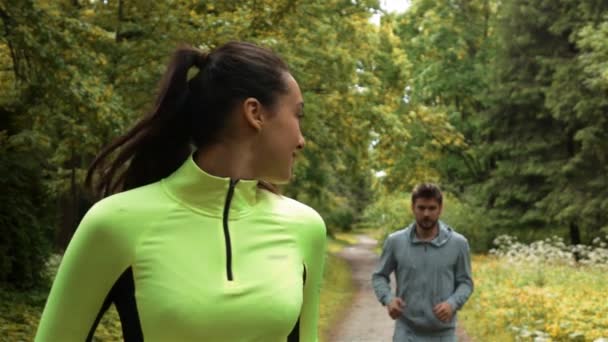 Жінка біжить назад до свого партнера, бігаючи і виграючи гонку в парку — стокове відео