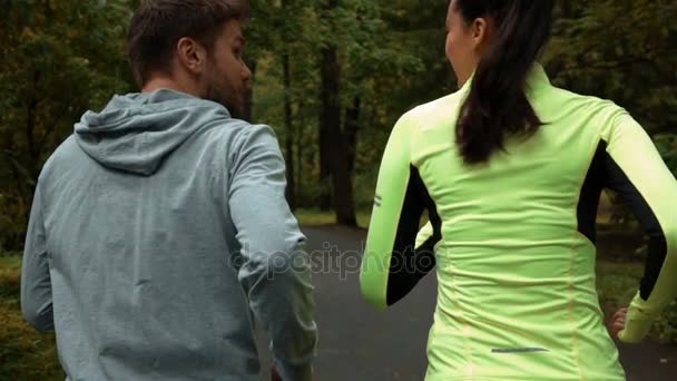 Vrouw en man communiceren en glimlachen tijdens ochtend joggen. Ze draaien op het park. — Stockvideo