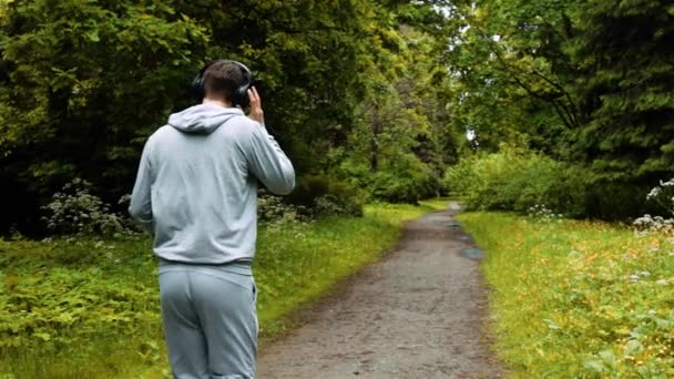 Mannelijke atleet in warme kleren in herfst park luisteren naar muziek en hood kleding. — Stockvideo