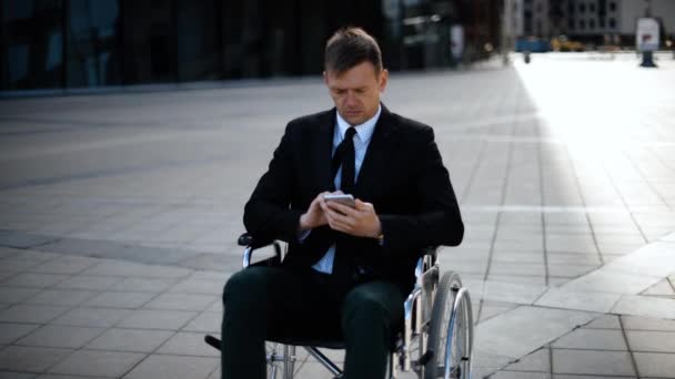 Giovane uomo d'affari seduto sulla sedia a rotelle sta giocando o lavorando con il suo smartphone — Video Stock