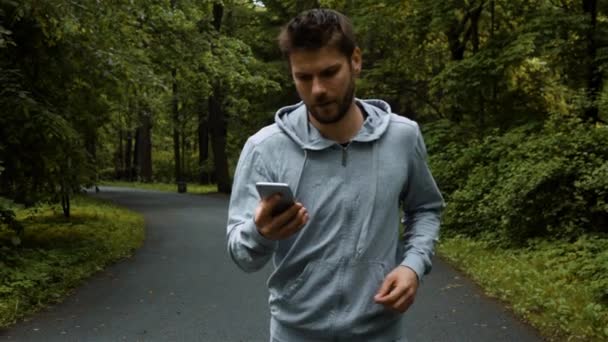 Joven corredor poderoso fuera en el parque natural de otoño con teléfono — Vídeo de stock
