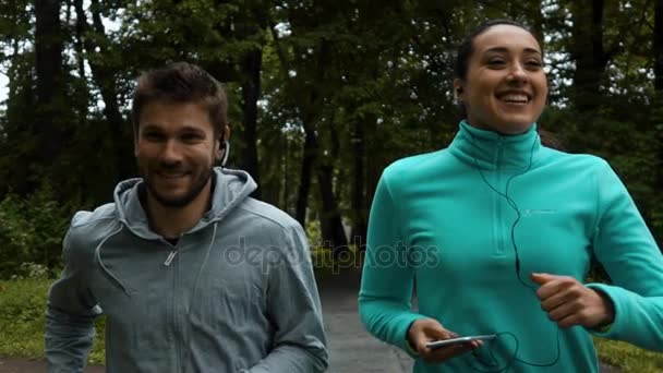 Ungt par kör tillsammans i parken med gadjets — Stockvideo