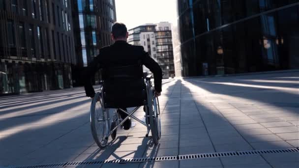 Back view of a invalid businessman in wheelchair moves in business district. — Stock Video