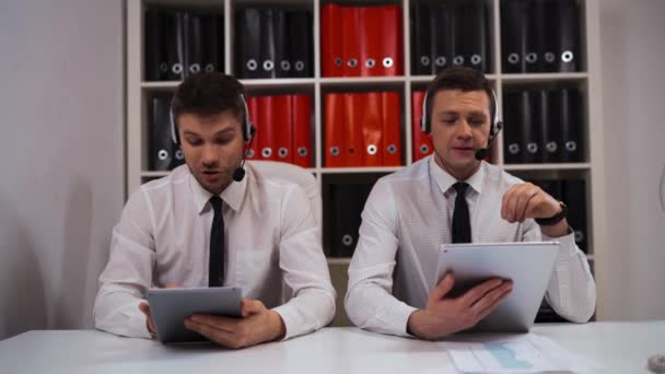 Two male in call-centre talking with customers by headsets. — Stock Video