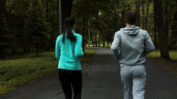 Два молодих бігунів синхронно біжать в осінньому парку — стокове відео