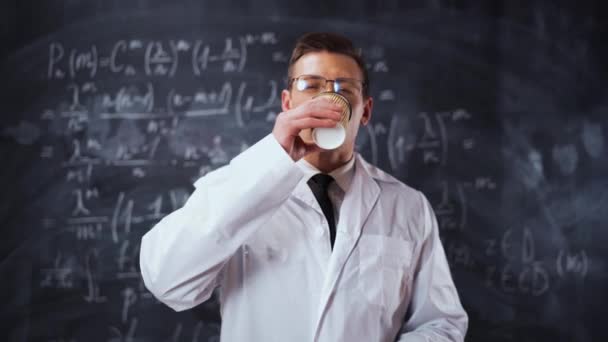 Вчений чоловік у білому робочому одязі біля крейдяної дошки з рівняннями п'є каву — стокове відео