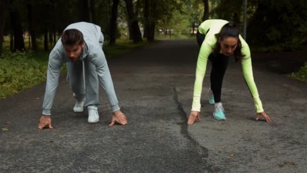 Fitness paar klaar voor het uitvoeren van de race op houten loopbrug op een outdoor park. — Stockvideo