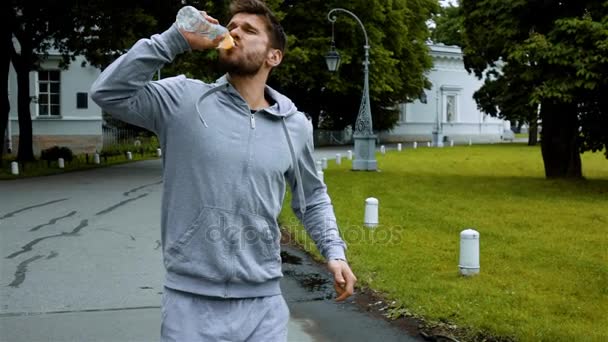 O desportista bebe água limpa da garrafa salpicando água . — Vídeo de Stock