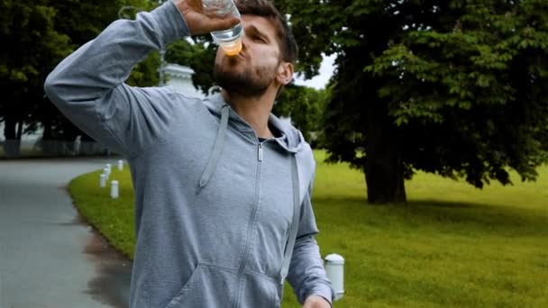 Fitness man dricksvatten från flaska stänkande vatten. — Stockvideo