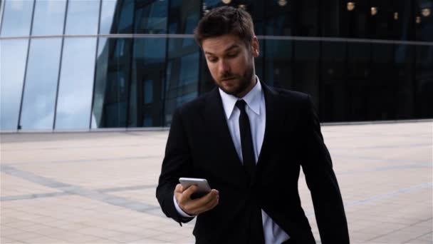 Νεαρός επιχειρηματίας γραπτών μηνυμάτων sms χρησιμοποιώντας app στο smart phone ενώ το περπάτημα στην πόλη — Αρχείο Βίντεο
