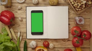 Masada içi boş yemek kitabına spatula ve akıllı telefon ile işaret eden kişi