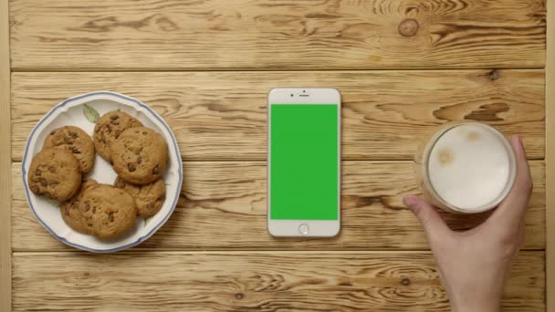 Περικοπή πρόσωπο πίνοντας καφέ και τρώγοντας cookies κοντά smartphone — Αρχείο Βίντεο