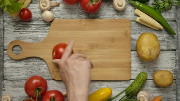Αρσενικό χέρι γυρίζοντας κόκκινη ντομάτα σε μια ξύλινη σανίδα. — Αρχείο Βίντεο