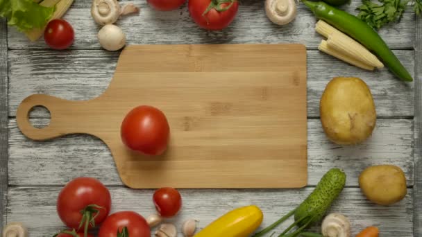 El tomate gira sobre una tabla de cortar de madera sobre una mesa rústica. — Vídeo de stock