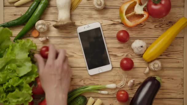 Mão masculina tomando smartphone da mesa com legumes — Vídeo de Stock