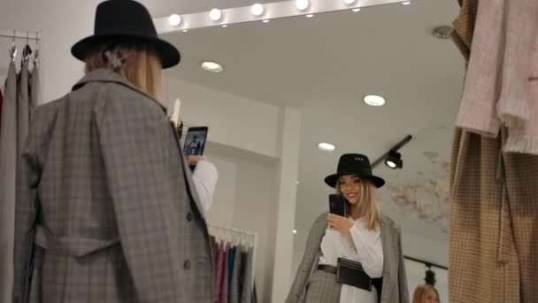 Stylische junge Frau macht Selfie in Umkleidekabine vor großem Spiegel moderner Boutique. — Stockvideo