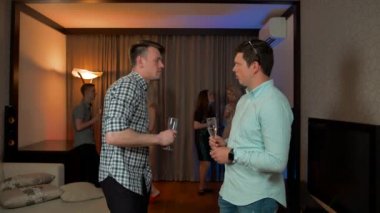 Erkek arkadaşlar şampanya içip apartman partisinde sohbet ediyorlar.