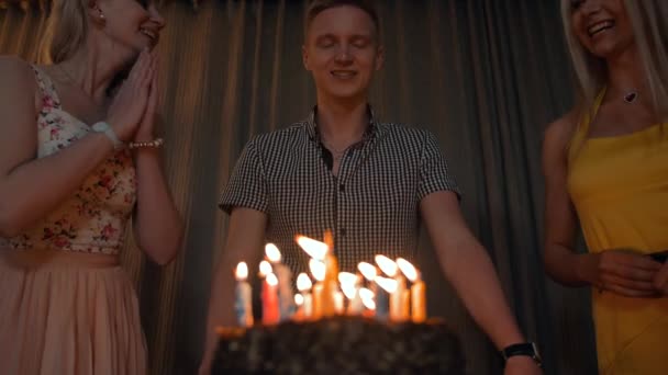 Young man blowing out much candles on a festive cake with girls near. — Stock Video