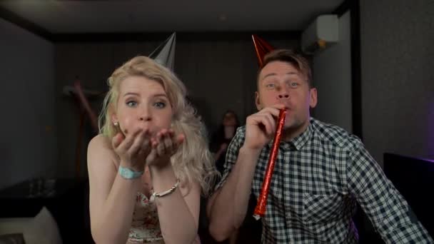Belo jovem casal se divertindo na festa soprando festa apitos confete — Vídeo de Stock
