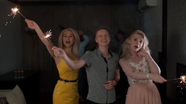 Egy csapat boldog ember, akik csillagszórókat tartanak a partin, táncolnak és mosolyognak.. — Stock videók