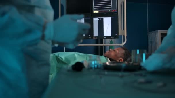 Paciente de pele escura na mesa cirúrgica no fundo das mãos dos cirurgiões — Vídeo de Stock