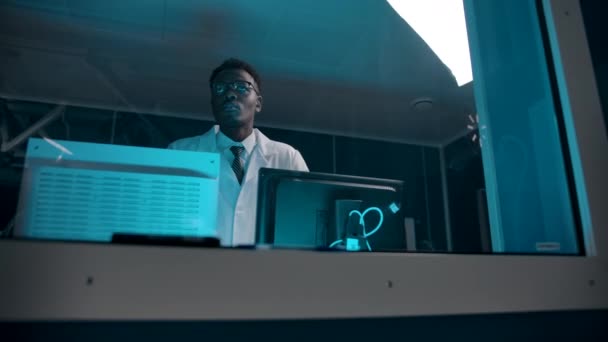 Zwarte huid arts in een witte badjas die toezicht houdt op de operatie vanuit de controlekamer. — Stockvideo