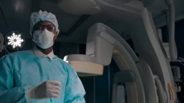 Profesyonel esmer cerrah ameliyattan sonra maskeyi çıkarır ve ellerini eldivenle gösterir.