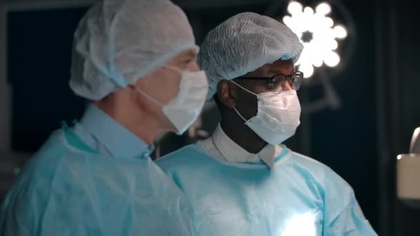 Многонациональные хирурги разговаривают в операционной — стоковое видео