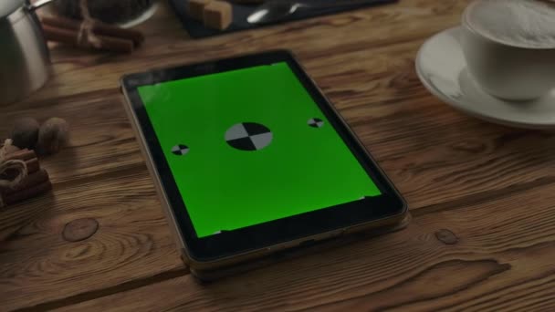 Цифровой планшет с вертикальным зеленым экраном на деревянном столе рядом с чашкой кофе на деревянном столе . — стоковое видео