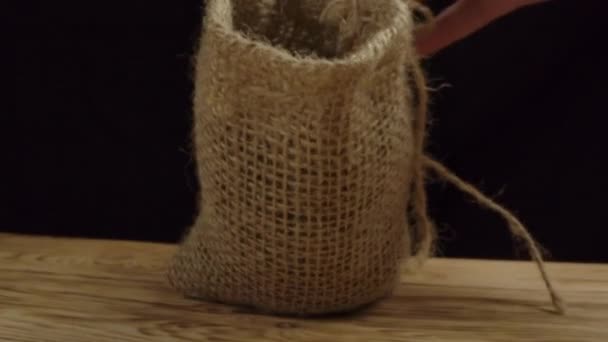 Geroosterde koffiebonen vallen neer met jute zak op houten tafel — Stockvideo