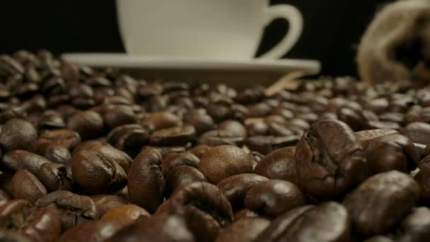 Camera verplaatsen gooien geroosterde koffiebonen naar witte klassieke koffiekop — Stockvideo