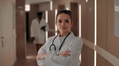 Gülümseyen kadın doktor hastane koridorundaki kameraya bakıyor.
