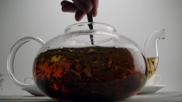 Stirring tea in a transparent teapot with spoon — Stock Video