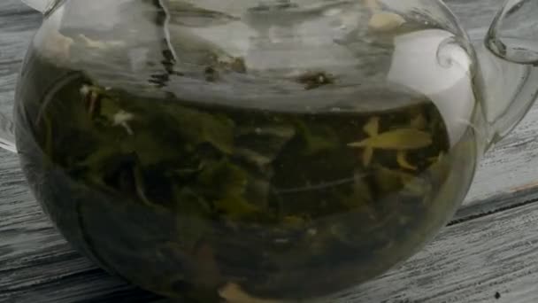 Míchání čaje s ovocem a květinami v konvici na dřevěném stole — Stock video