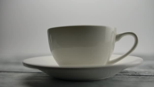 Menselijke hand zet een transparante theepot op de houten tafel achter klassieke beker — Stockvideo